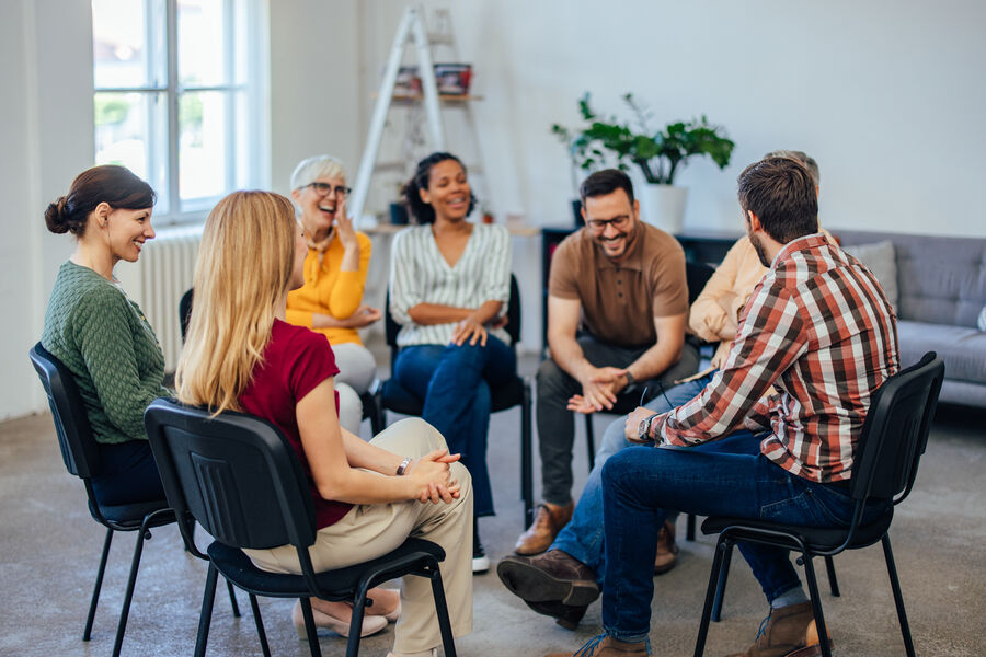 A circle of adults sitting together in a sunlit room, listening attentively